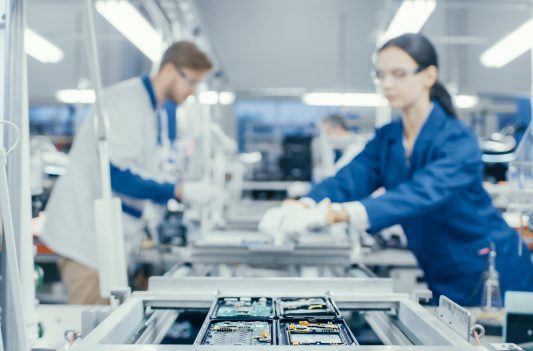 Shot of an Electronics Factory Workers Assembling Circuit Boards by Hand While it Stands on the Assembly Line. High Tech Factory Facility.